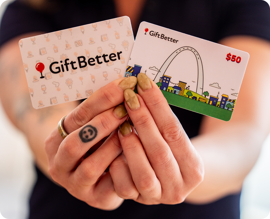 Hands holding up two GiftBetter gift cards, one showing the St. Louis Arch